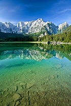 Julian Alps and coniferous forests of Planica valley reflected in lake, stones at bottom of lake in foreground. Zelenci Springs Nature Reserve, Slovenia. July 2007.