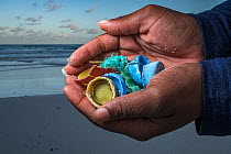 Plastic litter of bottle tops and fishing line held in hands of litter picker, washed up on beach. The Bahamas. 2020.
