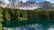 Latemar mountain range and coniferous forest reflected in Lago di Carezza. Dolomites, South Tyrol, Italy. June 2019.