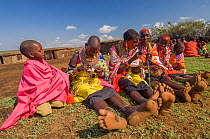 Maasai women creating traditional bead jewellery, children watching. Maasai Mara National Reserve, Kenya. 2007.