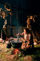 Valya Serotetto, a Nenets girl, stirs a pot of reindeer stew over an open fire in a tent. Yamal. Siberia. Russia.1993.