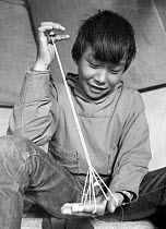 Magssanguak Imina making a traditional string puzzle that represents a tent, while sitting in a tent. Thule, Northwest Greenland. 1971