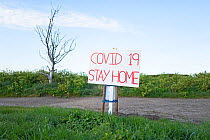 Sign with message requesting people stay at home during UK lockdown during Coronavirus pandemic. In parking area opposite Cley Marshes Norfolk Wildlife Trust Reserve, Norfolk, England, UK. April 2020