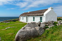 Traditional thatched cottage on coast, behind stonewall. Brinlack, Bloody Foreland, County Donegal. Republic of Ireland. June 2020.