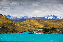 Pehoe Lodge on shore of Lake Pehoe, mountains beyond. Lake turquoise coloured due to glacial rock flour. Torres del Paine National Park, Patagonia, Chile. January 2020.