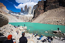 Tourists at lake below glacier and mountains including Torres del Paine rock peaks. Torres del Paine National Park, Patagonia, Chile. January 2020.