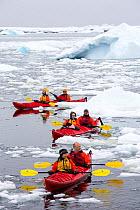 Tourists from expedition cruise ship sea kayaking amongst sea ice and icebergs. Off Vernadsky Station, Galindez Island, Antarctica. January 2020.