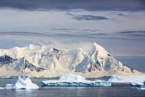 Snow covered coastal mountains viewed across icebergs in Southern Ocean. Detaille Island, Graham Land, Antarctica. January 2020.