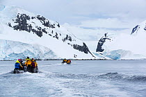 Tourists from expedition cruise ship in zodiacs heading towards mountains of Spert Island, Palmer Achipelago, Antarctica. December 2019.