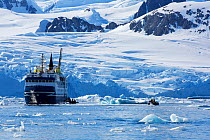 Expedition cruise ship moored off Petermann Island in Lemaire Channel, tourists in zodiacs. Antarctica. December 2019.