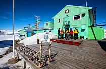 Tourists from expedition cruise ship visiting Vernadsky Station Ukrainian research base, dog sleds in foreground. Galindez Island, Argentine Islands, Antarctica. December 2019.