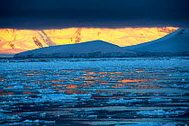 View across sea ice to Anvers Island, low cloud over mountains at sunset. Lemaire channel, Antarctica. December 2019.