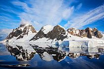 Snow covered peaks of Booth Island and sky reflected in Lemaire Channel, Antarctica. December 2019.