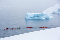 Tourists from an expedition cruise ship sea kayaking between icebergs and Portal Point. Reclus Peninsula, Antarctica. December 2019.