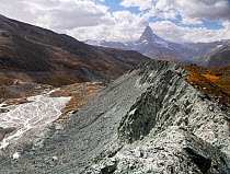 Lateral moraine deposited at edge of Findel glacier. Glacier in retreat with braided river in valley, Matterhorn in distance. Zermatt, Valais, Switzerland. September 2019.