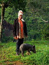 Papuan woman with domestic pig, portrait, rainforest in background. Bogo, Kerowagi District, Simbu Province, Papua New Guinea. 2019.