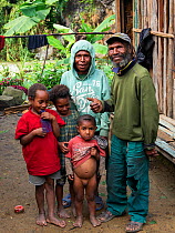 Papuan family beside house, portrait. Koronige River in background. Bogo, Kerowagi District, Simbu Province, Papua New Guinea. 2019.