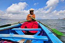 Aymara woman rowing a blue boat, Lake Titicaca, Bolivia. October.