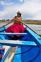 Aymara woman rowing a blue boat, Lake Titicaca, Bolivia. October.
