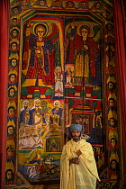 Young priest standing in front of mural paintings in the sanctum of Ura Kidane Mehret, an Ethiopian Orthodox Church. Zege Peninsula, Ethiopia. 2018.