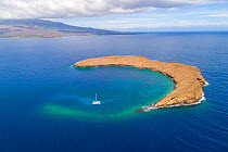 Molokini Crater, aerial shot of the entire crescent shaped islet with one charter sailboat boat and the island of Maui in the background, Hawaii.
