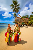 Girls in traditional dress worn for cultural ceremonies on tropical beach, hut and palm trees in background. Yap, Micronesia. 2013. Model released.
