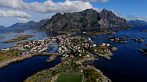 An aerial shot panning up to reveal a coastal landscape with football field, houses and mountains in the background, Henningsver, Lofoten, Norway, August.