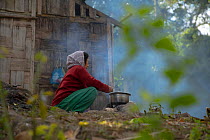 Local elderly woman cooking a meal from her family over open fire (with wood from local forest) Abor hills, Arunachal Pradesh, India, December 2019.  The locals are also known to construct their hou...