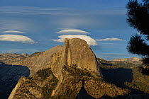 Half Dome in evening light, tourist standing on peak in foreground with arms outstretched. Yosemite National Park, California, USA. September 2013.