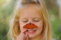 Girl smiling with Gulf fritillary (Agraulis vanillae) resting on her nose, portrait. Hill Country, Texas, USA. 2013. Model released.