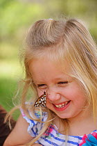 Girl laughing with Gulf fritillary (Agraulis vanillae) resting on her nose, portrait. Hill Country, Texas, USA. 2013. Model released.