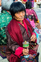 Buddhist woman with prayer beads and spinning hand prayer wheel at Thimphu Tsechu Festival. Bhutan. September 2013.
