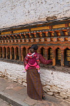 Woman with baby on back spinning prayer wheels at Changangkha Lhakhang Monestary, &#39;The Fertility Temple&#39;. Bhutan. September 2013.