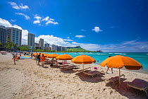 A view of beach chairs, umbrellas and tourists on the iconic Waikiki beach with Diamond Head behind on the island of Oahu, Hawaii. June 2016.
