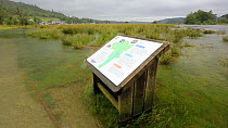 A park information board partially submerged underwater due to the River Brathay completely over flowing following a June record amount of rain falling in 24 hours, Ambleside, Lake District, UK.
