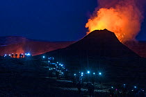 Long line of walking people with headlights, heading back at night from visiting Fagradalsfjall volcano on Iceland, photographed around half an hour after sunset. The eruption draws large numbers of v...