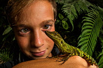 Teenage boy looking at an Equatorial anole (anolis aequatorialis) on his hand. Mind, Ecuador. Amazon Rainforest. Model released.