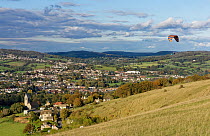 Paraglider flying from Selsley Hill, with Selsley village and Stroud in the background, Gloucestershire, UK, October.