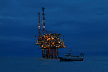 Fishing vessel &#39;Ocean Harvest&#39; passing the &#39;Draupner&#39; oil platform lit up at night,  North Sea. July 2020.