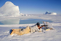 Concealed behind a white linen screen, Inuit hunter Jeremias Petersen, shoots at a seal on the sea ice near Savissivik. Northwest Greenland. (1997)