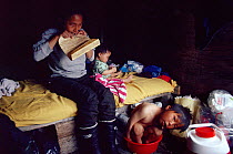 Panerak, an Inuit woman chewing on a piece of bearded sealskin to soften it before sewing to make the soles for a pair of Kamik boots, with her two children inside a tent at a Spring hunting camp, Nug...