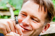 Naturalist and presenter Chris Packham holding a Stag beetle (Lucanus cervus) during filming for BBC programme &#39;Animals Guide to Britain&#39;, Richmond Park, London, UK. 2010.