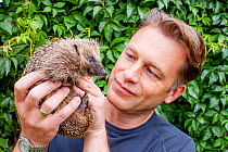 Naturalist and presenter Chris Packham holding a European hedgehog (Erinaceus europaeus) during filming for BBC programme &#39;Animals Guide to Britain&#39;, 2010.