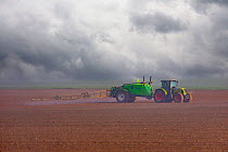 Spraying chemicals onto  field using a wide farm sprayer behind a tractor, Oise, France. April