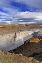 Dettifoss waterfall with rainbow, in Vatnajokull National Park in Northeast Iceland. Eary spring run-off, with snow pack colored with lava dust. The falls drop 44 metres (144 ft).