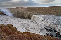 Dettifoss waterfall in Vatnajokull National Park, Northeast Iceland. Early spring run-off, with snow pack coloured with lava dust. The falls drop 44 metres (144 ft).