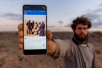 Biologist showing how poachers in the Sahara desert use social networks to share crimes on their mobile phones, Southern Morocco, Africa, March, 2020.