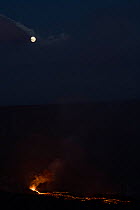 A full moon drops low in the sky before dawn as hot lava flows from Halemaumau Crater, Kilauea Volcano, Hawaii Volcanoes National Park, Hawaii Island, Hawaii, USA October, 2021.