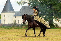 Woman in medieval costume riding side-saddle  on PRE Spanish horse, Chateau du Plessis-Bourre, Loire Valley, France.  2021