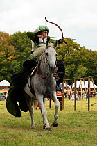 Woman riding side-saddle in medieval costume, firing arrow from a horse bow, Chateau du Plessis-Bourre, Loire Valley, France.  2021